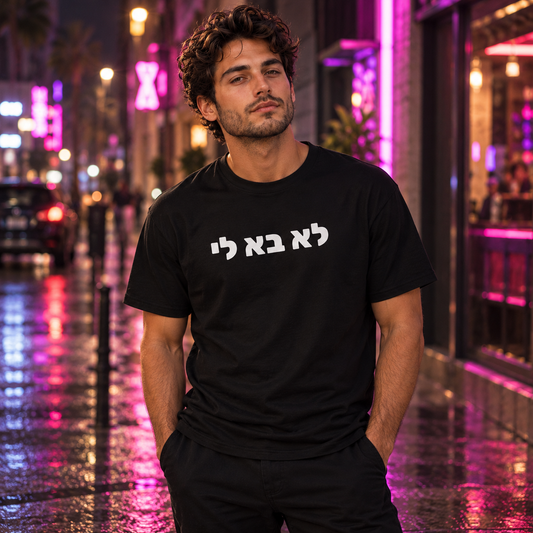 Tomer wearing the black MEEHAL לא בא לי tee on a neon-lit street at night